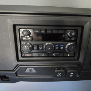 Dashboard control panel of a Mack PR64T76H showing various buttons and knobs, including power, climate, media, and settings controls.