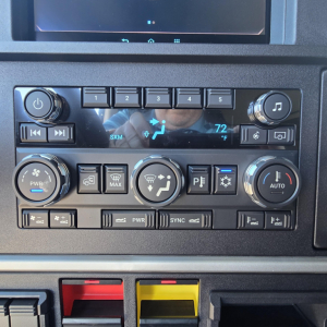 Dashboard controls of a 2026 Mack PR64T76H showing climate and media controls, knobs, and labeled buttons.