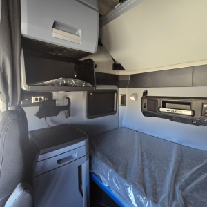Mack PR64T76H sleeper cab interior showing storage shelf, mounted monitor, and bed area with blue bedding.