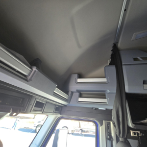 Interior view of a Mack PR64T76H truck cabin highlighting overhead storage compartments and ladder-like steps near the driver's seat.