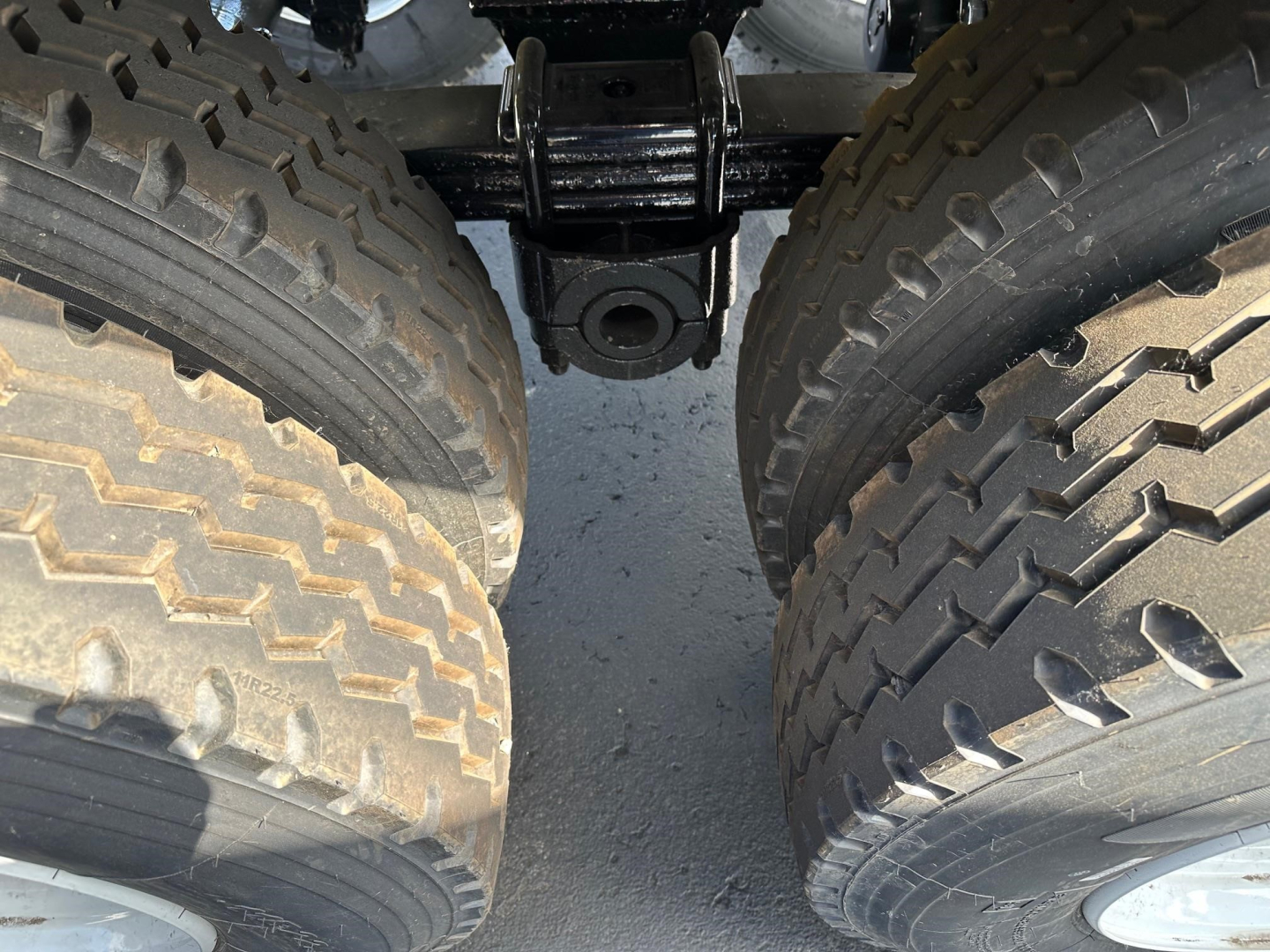 Dual rear truck tires and undercarriage showing suspension and hitch assembly for a dump trailer.