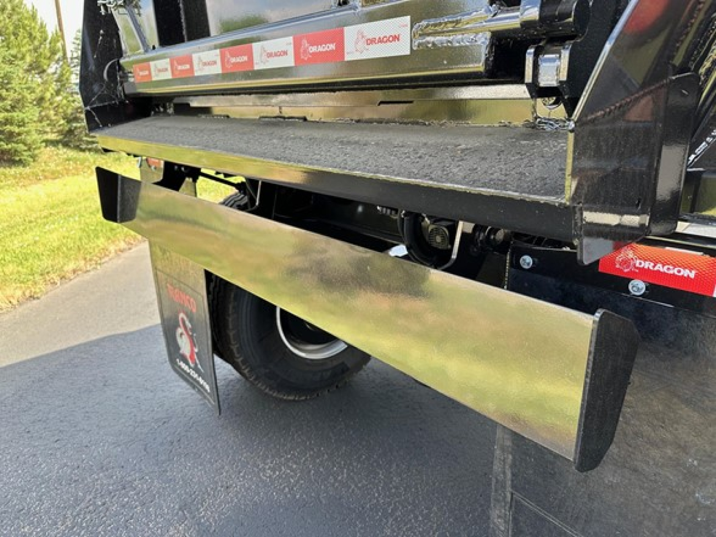 Vehicle tail section showing a shiny metal side panel and rear bumper of a 2025 Ranco quarter frame end dump trailer with branding stickers along the top rail.