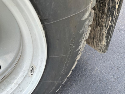 Wheel and tire of a trailer showing black tire with white rim and a mud flap; tire sidewall text partially visible.