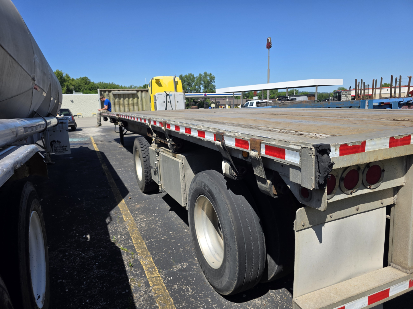 Flatbed trailer showing rear and side of a 2007 Fontaine Phantom with a long wooden deck, dual rear axles, and reflective safety tape.