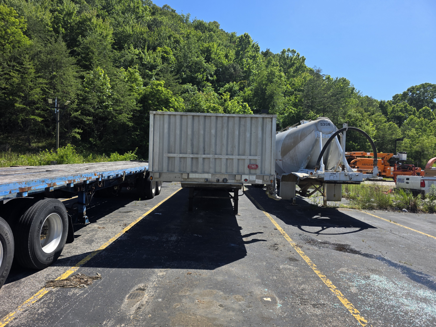 Flatbed trailer with a mounted concrete mixer on a Fontaine Phantom trailer at a lot, trees in background.