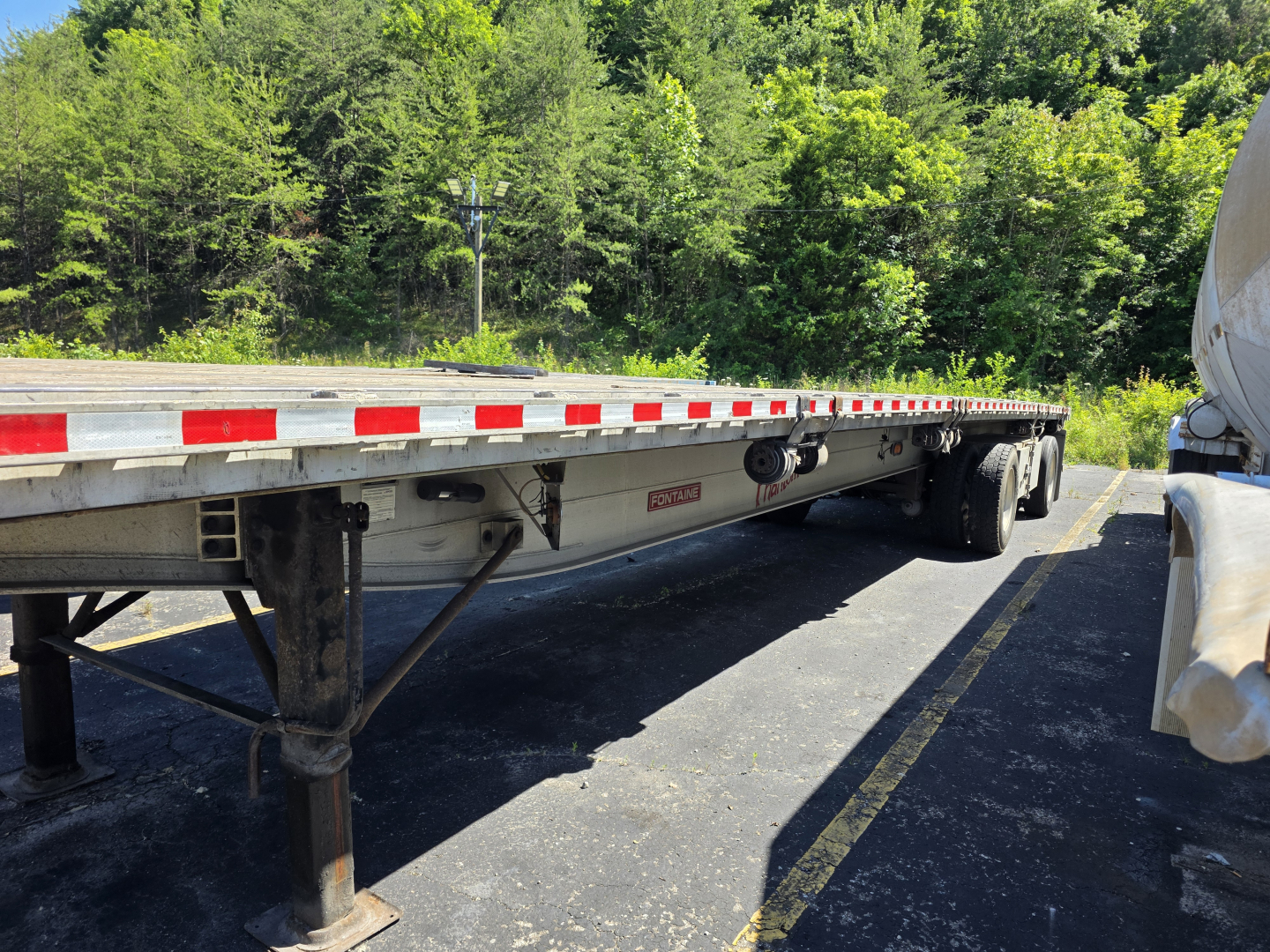 Flatbed trailer showing long PHANTOM deck with side railings and landing gear, Fontaine tag visible undercarriage near center, trees in background.