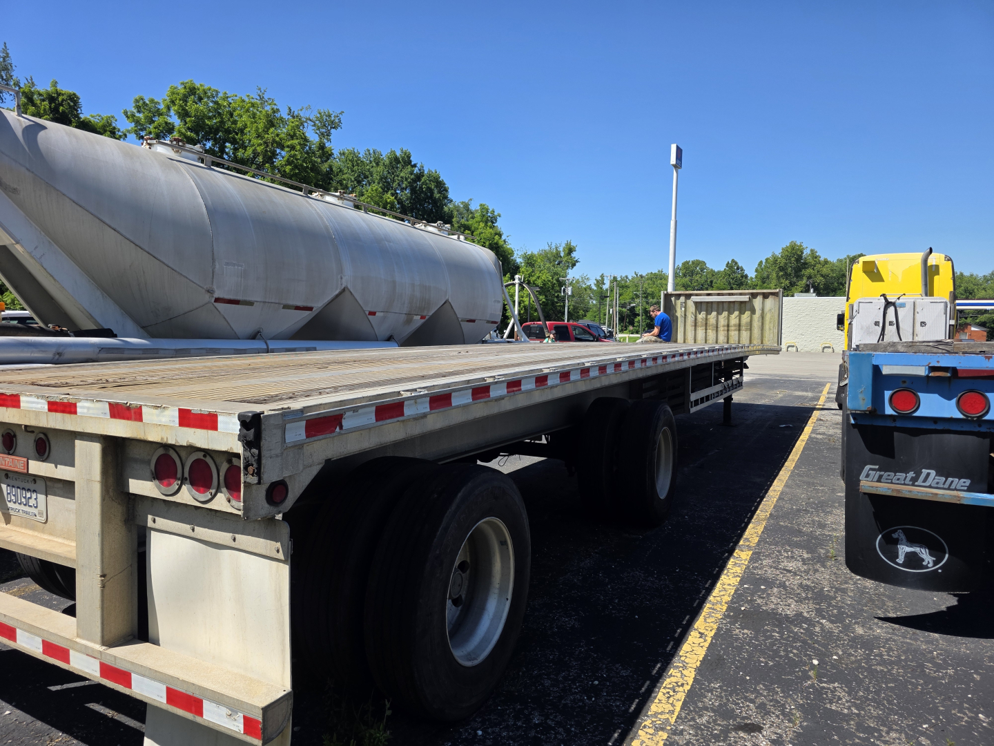 Flatbed trailer with dual rear axles and a large cylindrical tanker on a Fontaine Phantom trailer. Visible text on the kingpin area and reflective striping along the sides.