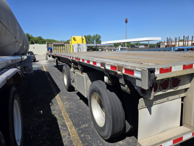 Flatbed trailer showing rear and side of a 2007 Fontaine Phantom with a long wooden deck, dual rear axles, and reflective safety tape.