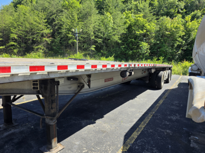 Flatbed trailer showing long PHANTOM deck with side railings and landing gear, Fontaine tag visible undercarriage near center, trees in background.