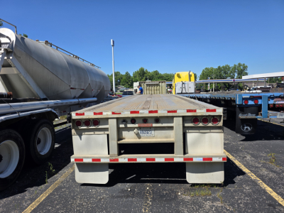 Flatbed trailer rear view showing taillights, reflective tape, and license plate on a Fontaine Phantom trailer in a parking lot.