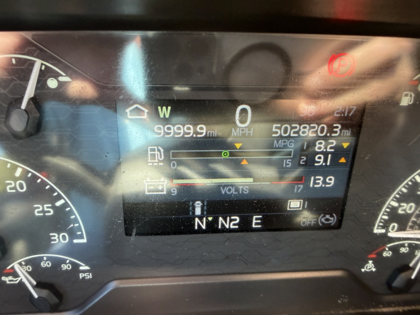 Volvo VNL dashboard display showing mileage and gauge readouts including speed 0 MPH, 9999.9 miles, fuel economy 8.2 MPG, battery volts 13.9, and gear indicator N° N N E.
