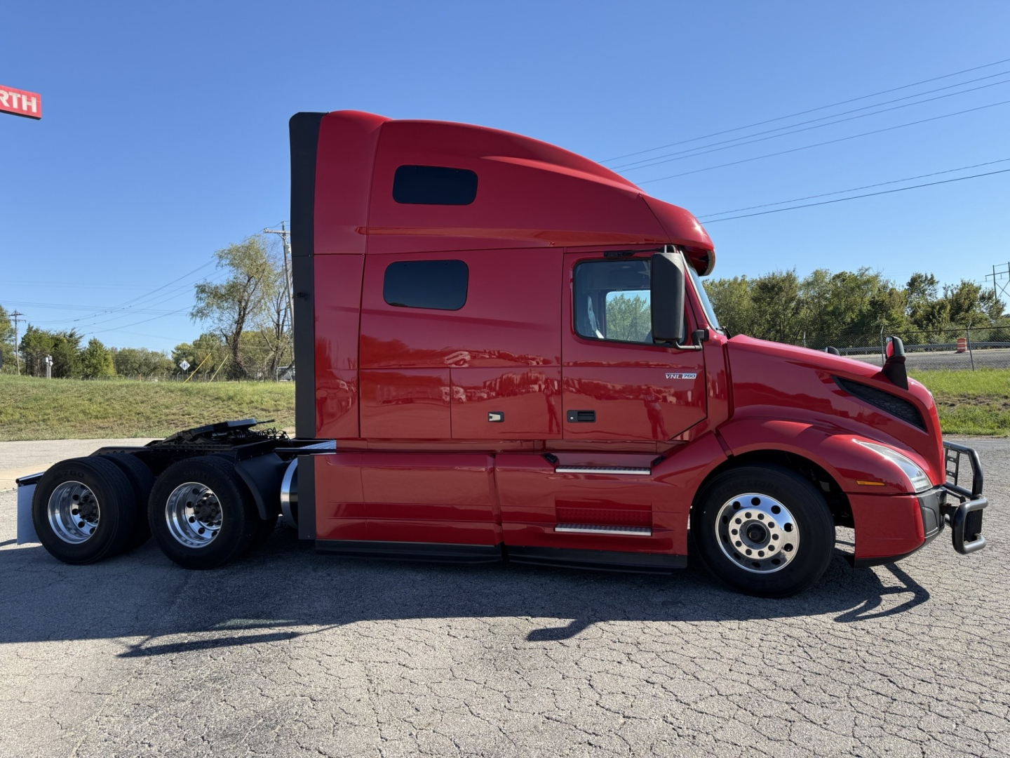 Truck side view showing a red 2021 Volvo VNL64T760 tractor with sleeper cab, chrome wheels, and black chassis. VIN 4V4NC9EH4MN283712 visible on listing.