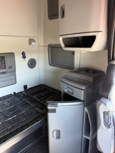 Interior cab area of a 2021 Volvo VNL truck showing driver seat, storage compartments, and a small refrigerator/drawer under dash.