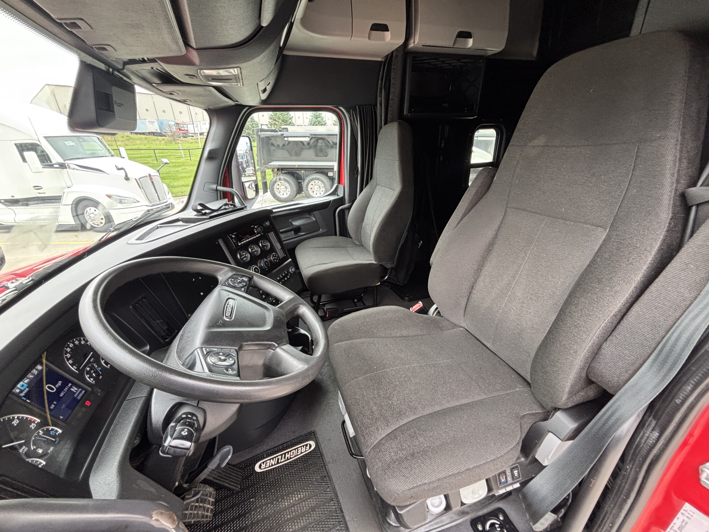 Cab interior of a Freightliner PT126064ST truck showing steering wheel, dashboard, driver seat, and passenger seat.