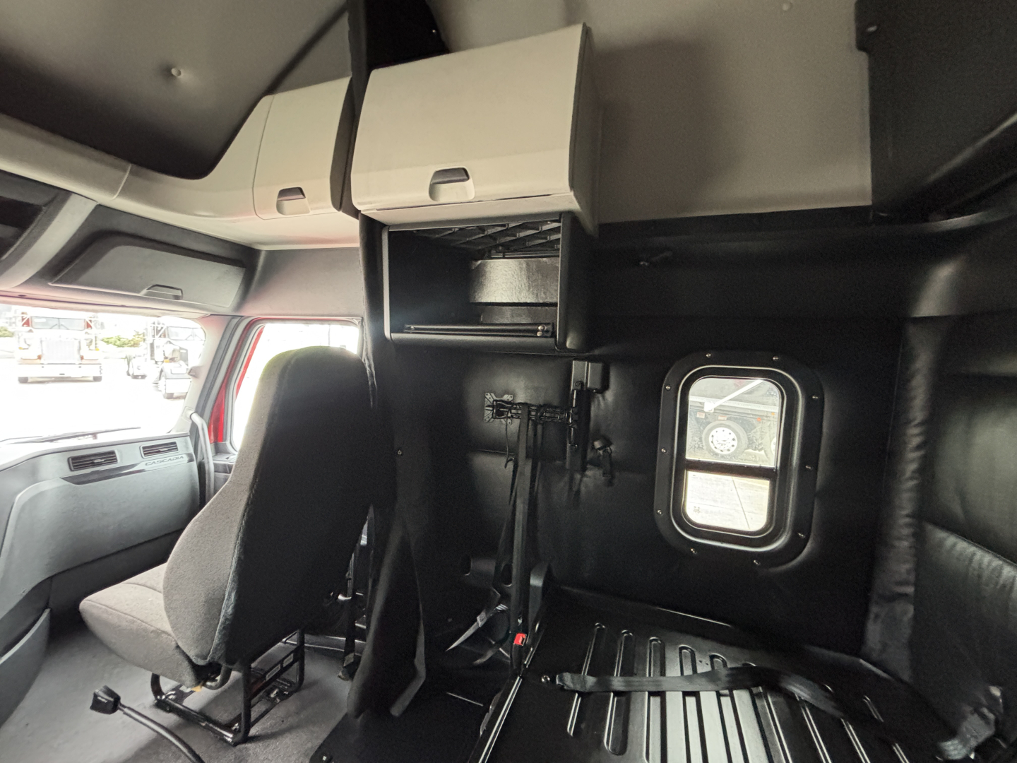 Truck sleeper cab interior with overhead cabinets and seat, window and gear area visible.