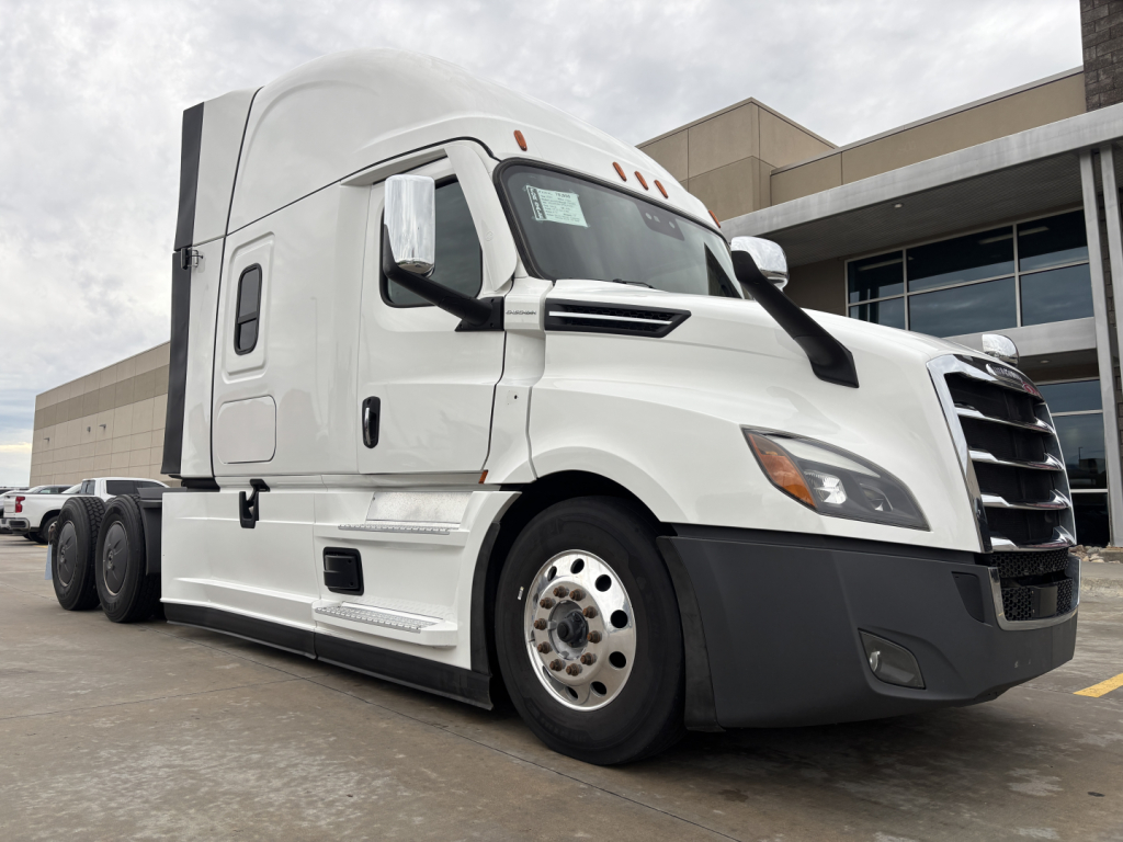 Truck front-left view showing Freightliner PT126064ST with sleeper cab, VIN 3AKJHHDV3PSUF5587 visible on window sticker; stock number 0633388 in a dealership lot.