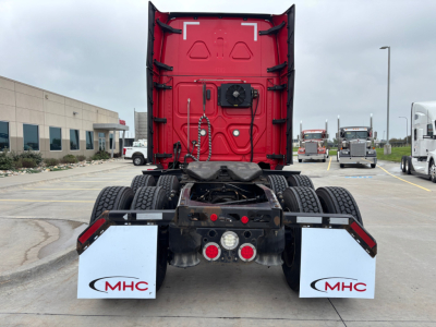 Rear view of a Freightliner truck tractor with red sleeper cab, black chassis, dual rear wheels, white MHC mud flaps. Visible text on mud flaps: MHC.