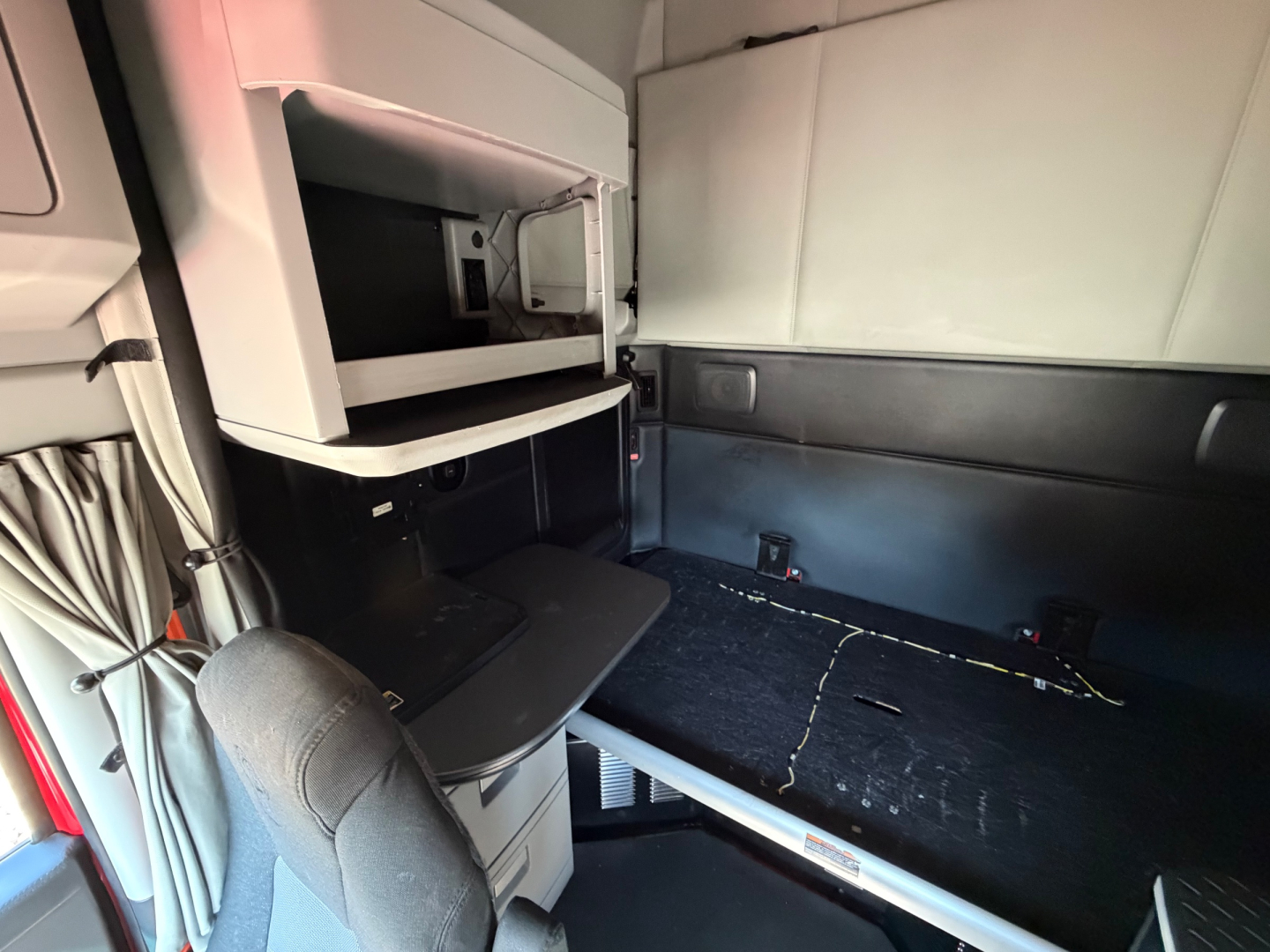 Kenworth T680 cab interior with sleeper area and bunk bed platform, storage compartments, and windowed bulkhead.