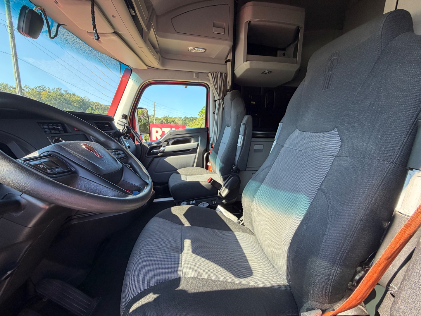 Kenworth T680 truck interior front cab view showing driver seat and passenger seat with dashboard, steering wheel, and overhead compartments.
