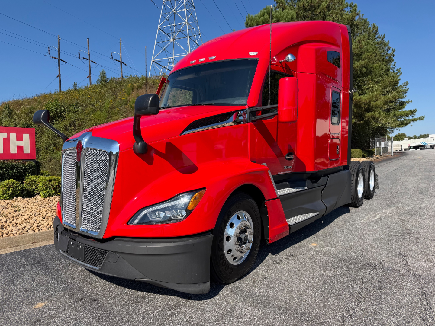 Kenworth T680 tractor in red side view showing front grille, headlights, and sleeper cab with banner-style windshield.