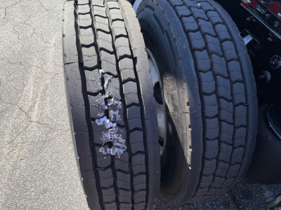 Kenworth T680 truck axle with dual rear tires; visible tread wear and a damaged left inner tire showing wear and possible coating.