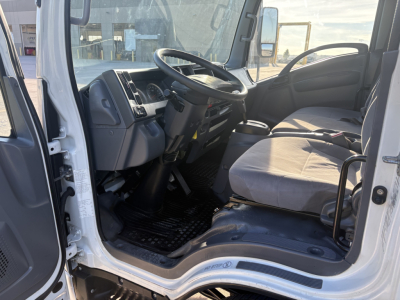 Isuzu NPR cab interior showing steering wheel, dashboard, and driver seat with gray cloth upholstery.