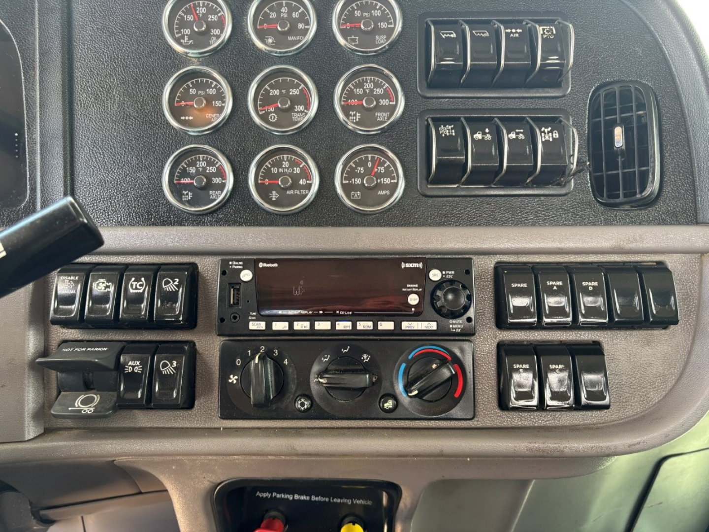 Panel of a Peterbilt 389 dash showing multiple gauges, switches, and climate controls with a radio unit in the center.