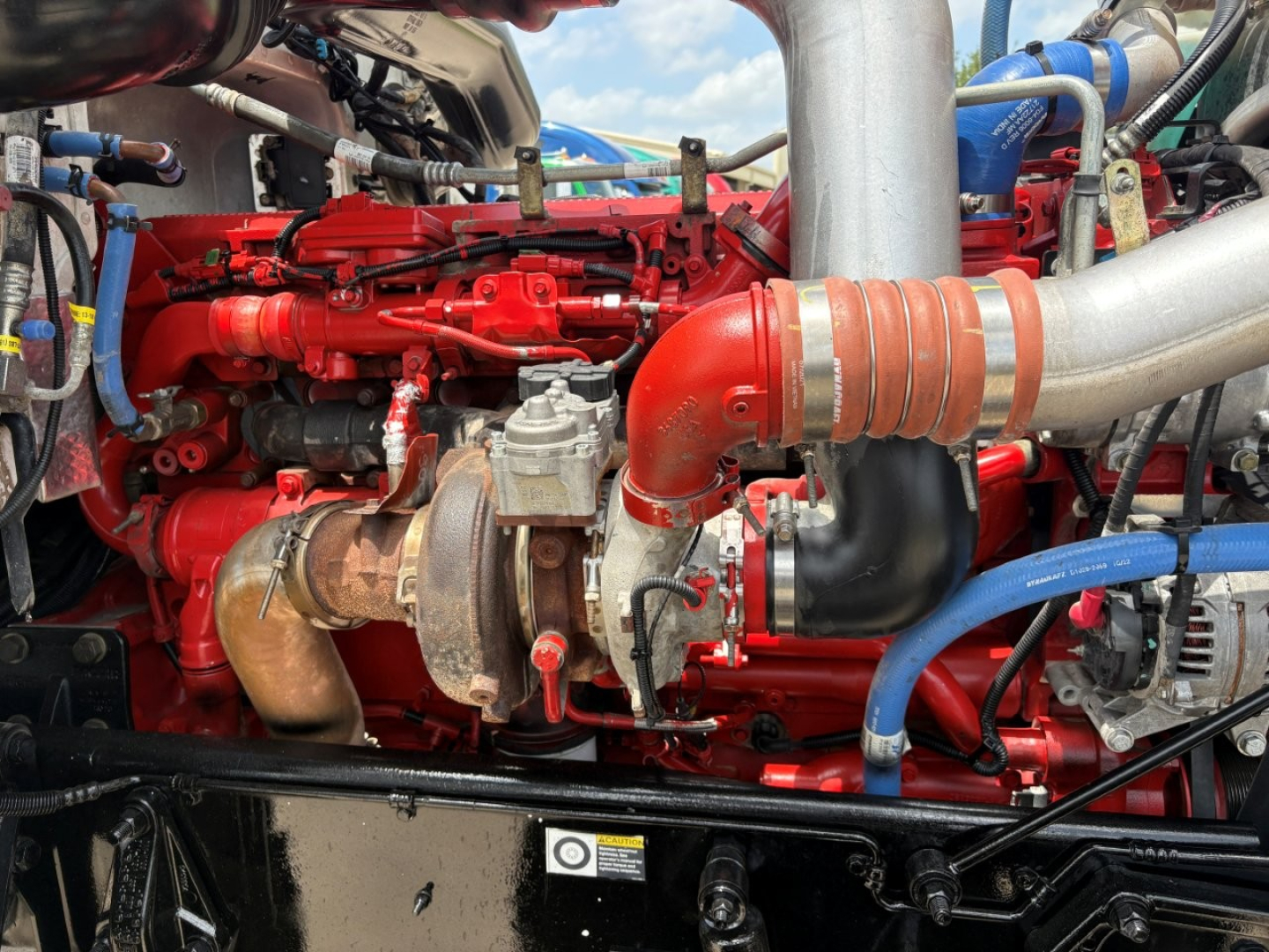 Peterbilt 389 engine bay showing red turbocharged diesel engine with intake piping and components.