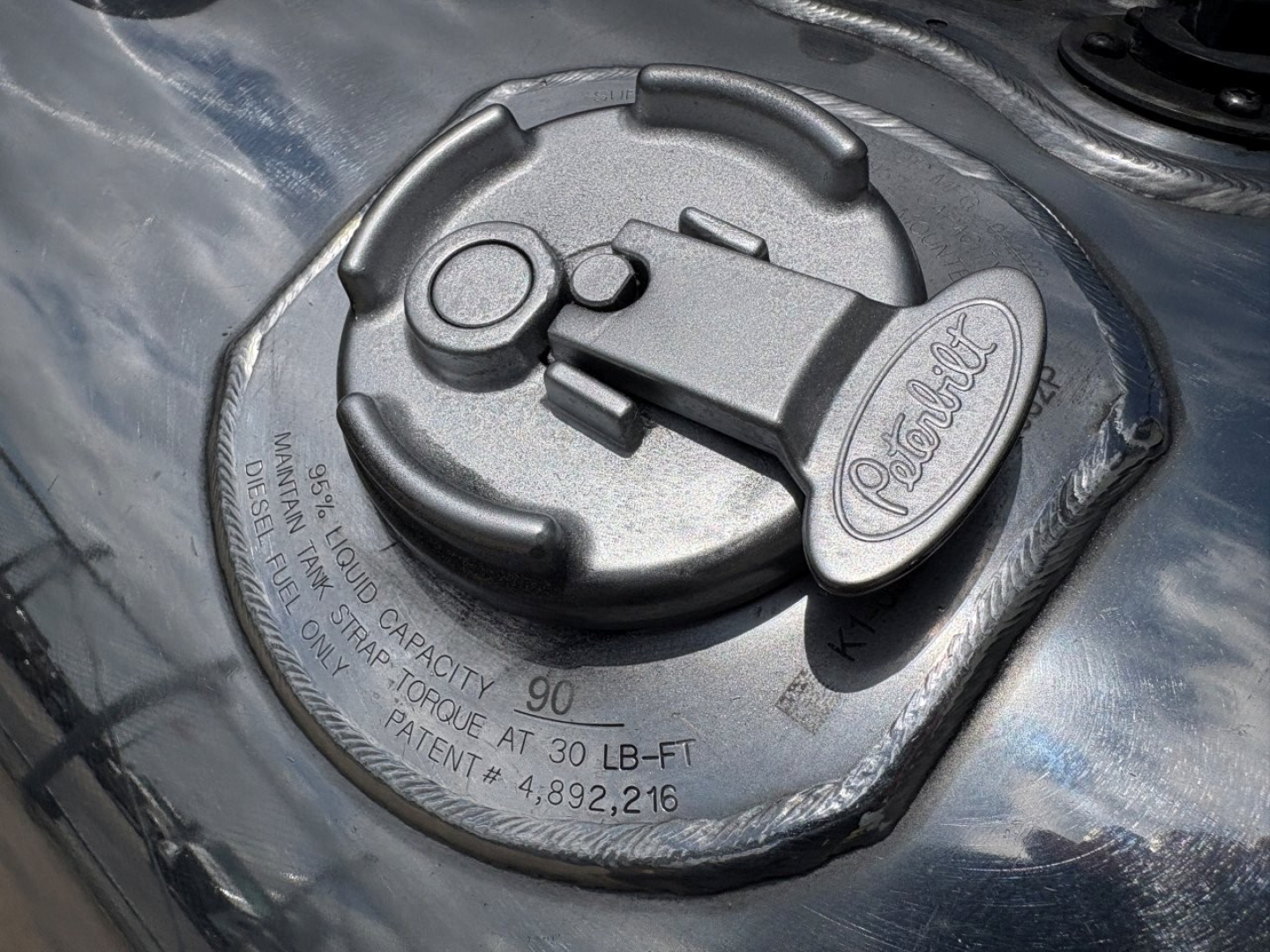 Peterbilt fuel tank cap on a 2023 Peterbilt 389 conventional daycab showing fuel cap with embossed Peterbilt logo and capacity markings.