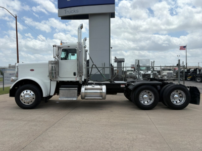 Peterbilt 389 conventional daycab tractor side view showing white cab, chrome exhaust stacks, fuel tanks, and dual rear axles.