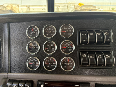 Peterbilt 389 dash panel with multiple gauges including air pressure, engine temperature, oil pressure, tachometer, and switch panels.