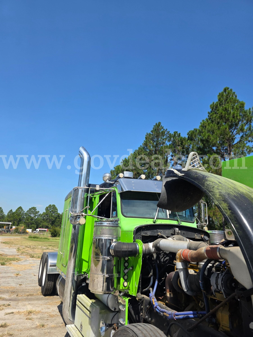Green Peterbilt 359 engine bay showing exposed hydraulic lines and chrome fuel tanks with tall exhaust stacks.