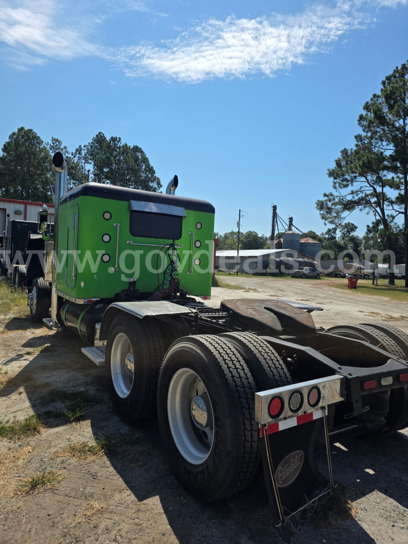 Peterbilt 359 tractor truck in green cab, rear view showing fifth wheel and dual rear wheels with mud flaps and trailer hooks.