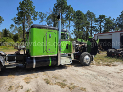 Peterbilt 359 green cab with sleeper, exposed engine bay, side exhaust stacks, rear chassis and wheel area visible in a yard.