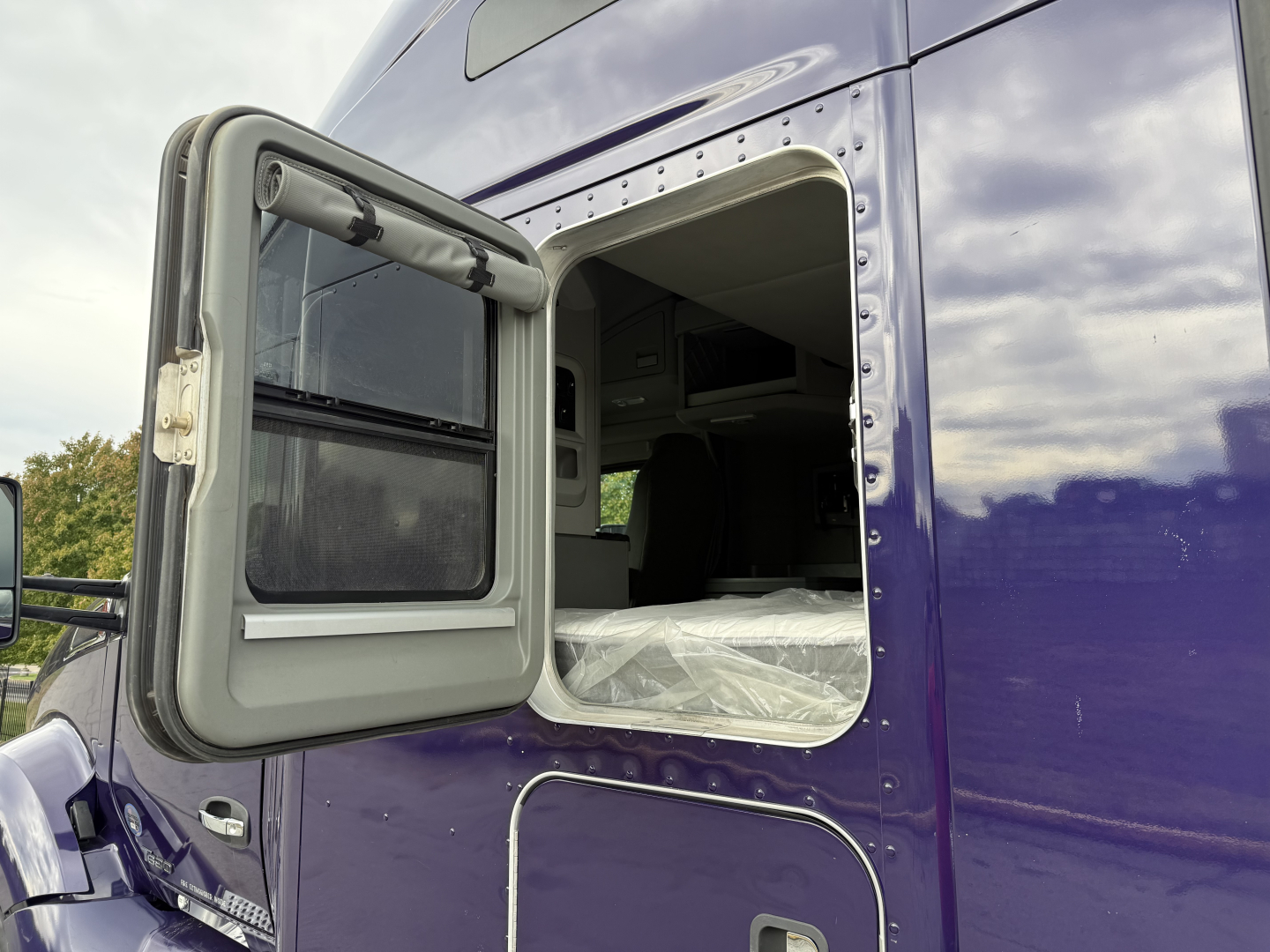 Kenworth T680 truck cab door open showing sleeper compartment exterior with glossy blue paint