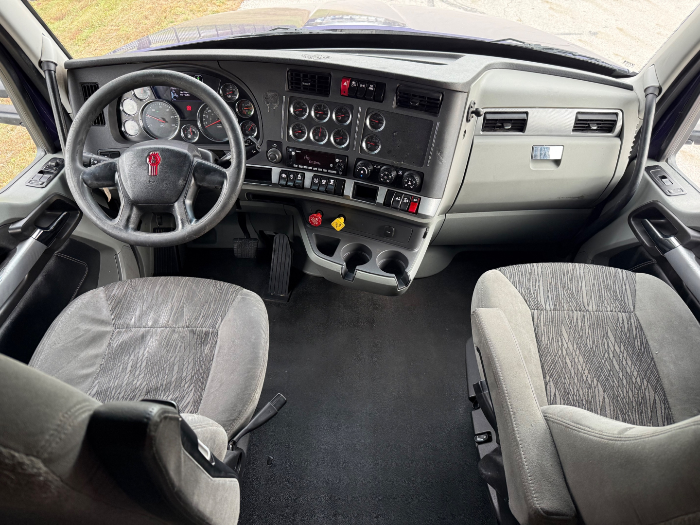 Kenworth T680 truck cab interior showing dashboard, steering wheel with Kenworth emblem, gauges, center console, and two front seats.