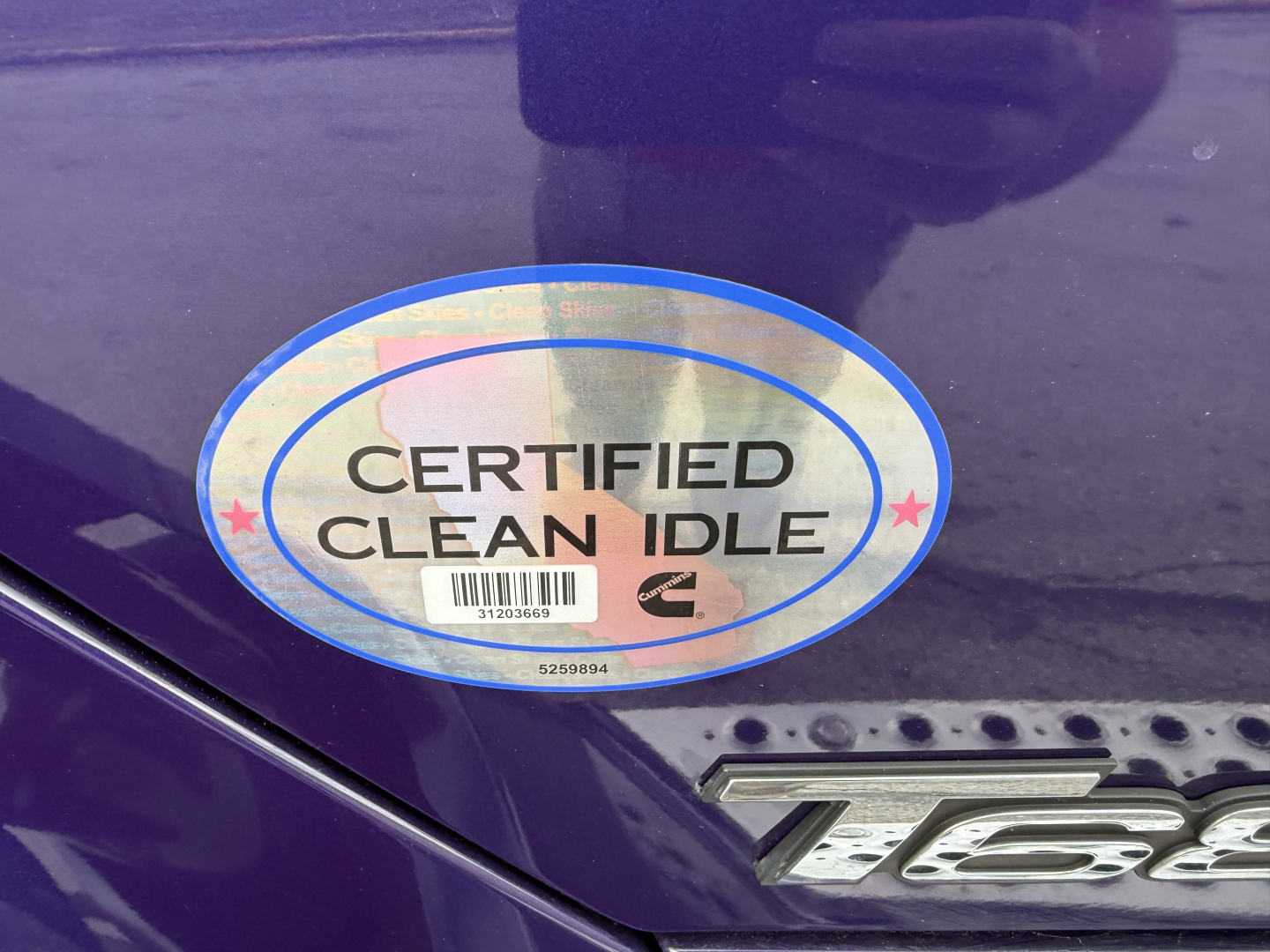 Kenworth T680 badge area with Certified Clean Idle sticker on a dark blue surface.