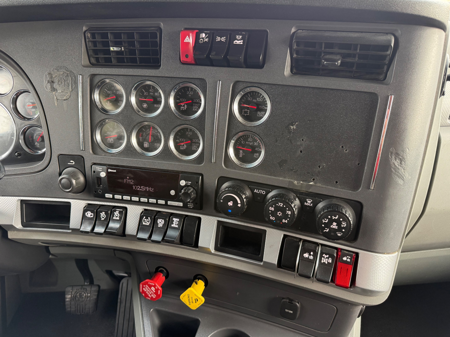 Dashboard panel of a 2021 Kenworth T680 showing multiple round gauges, air control switches, ignition area, and red/yellow key lanyards.