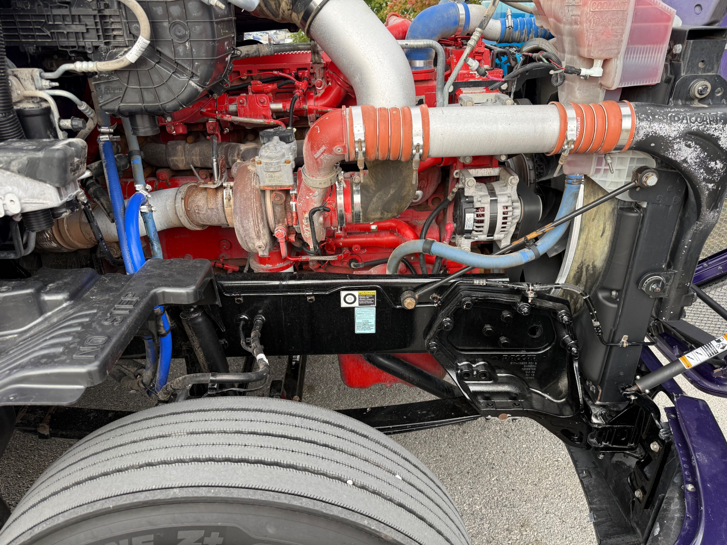 Kenworth T680 engine bay showing diesel engine components, hoses, radiator, and front frame with label plate.