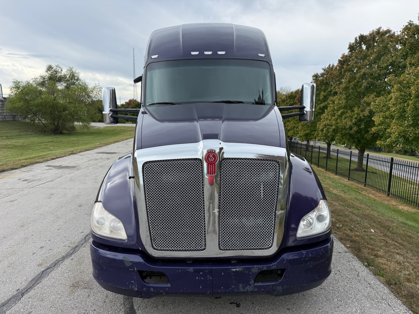 Kenworth T680 front view showing large chrome grille with emblem, dark blue cab, and bumper; side mirrors visible; daytime outdoor setting.