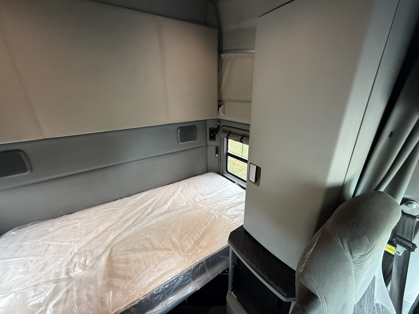 Kenworth T680 sleeper cab interior with bed in foreground and storage cabinet.
