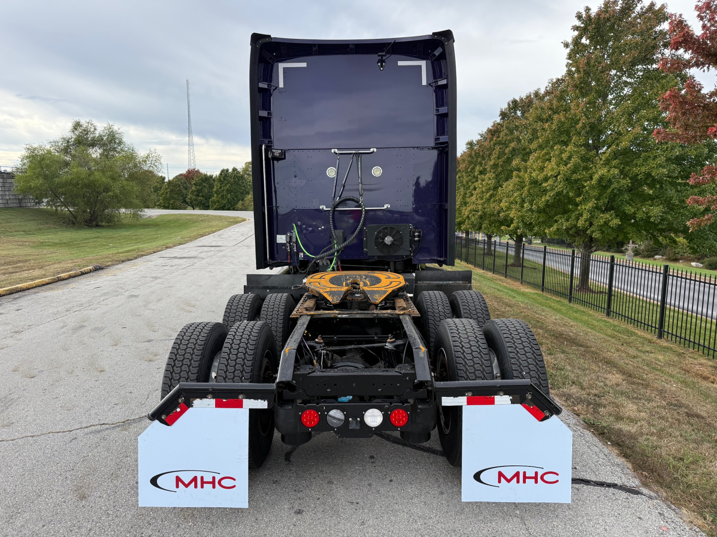 Kenworth T680 rear view showing fifth wheel, dual rear axles, mud flaps with MHC logos, and drivetrain area.