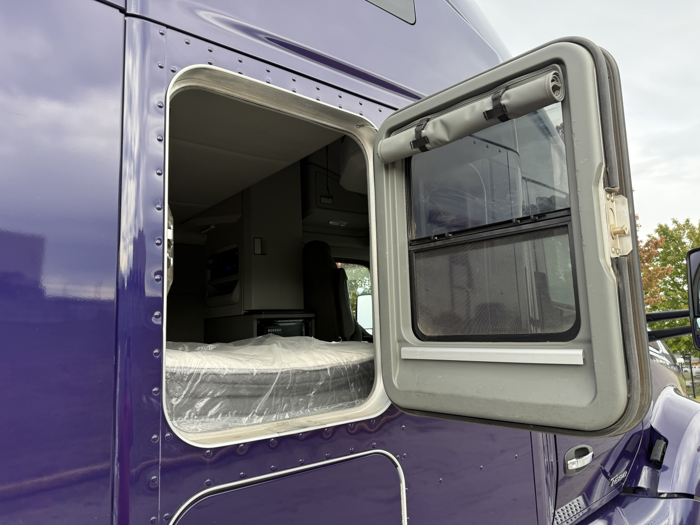 Kenworth T680 side view showing an open sleeper cab window and exterior purple paint