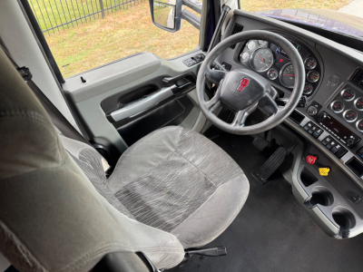 Cab interior of a 2021 Kenworth T680 shows steering wheel, dashboard with gauges, and driver seat; view from passenger seat.