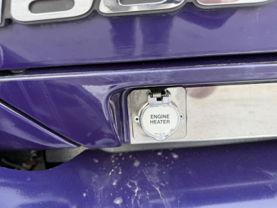Kenworth T680 rear showing engine heater access panel on purple bumper with small cap and latch