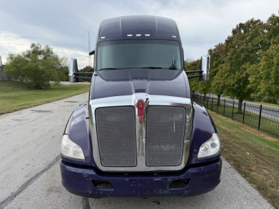Kenworth T680 front view showing large chrome grille with emblem, dark blue cab, and bumper; side mirrors visible; daytime outdoor setting.