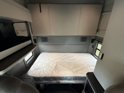 Kenworth T680 sleeper cab interior with bed, cabinets, and window; compact bunk area visible.