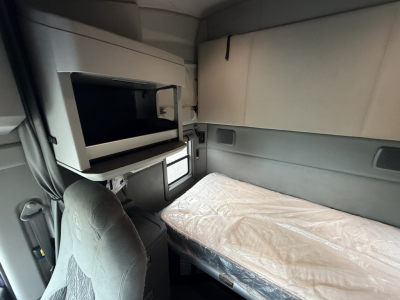 Truck cab interior showing sleeper bunk with mattress and mounted microwave oven above, side storage compartments, and window, in a 2021 Kenworth T680.