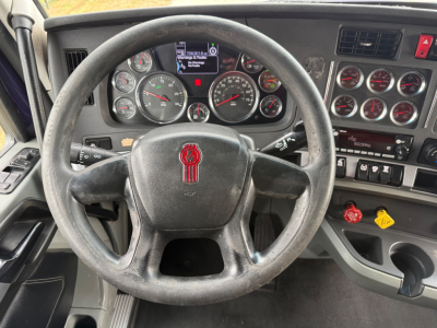 Steering wheel and instrument cluster of a 2021 Kenworth T680 truck interior with multiple gauges and control panels.