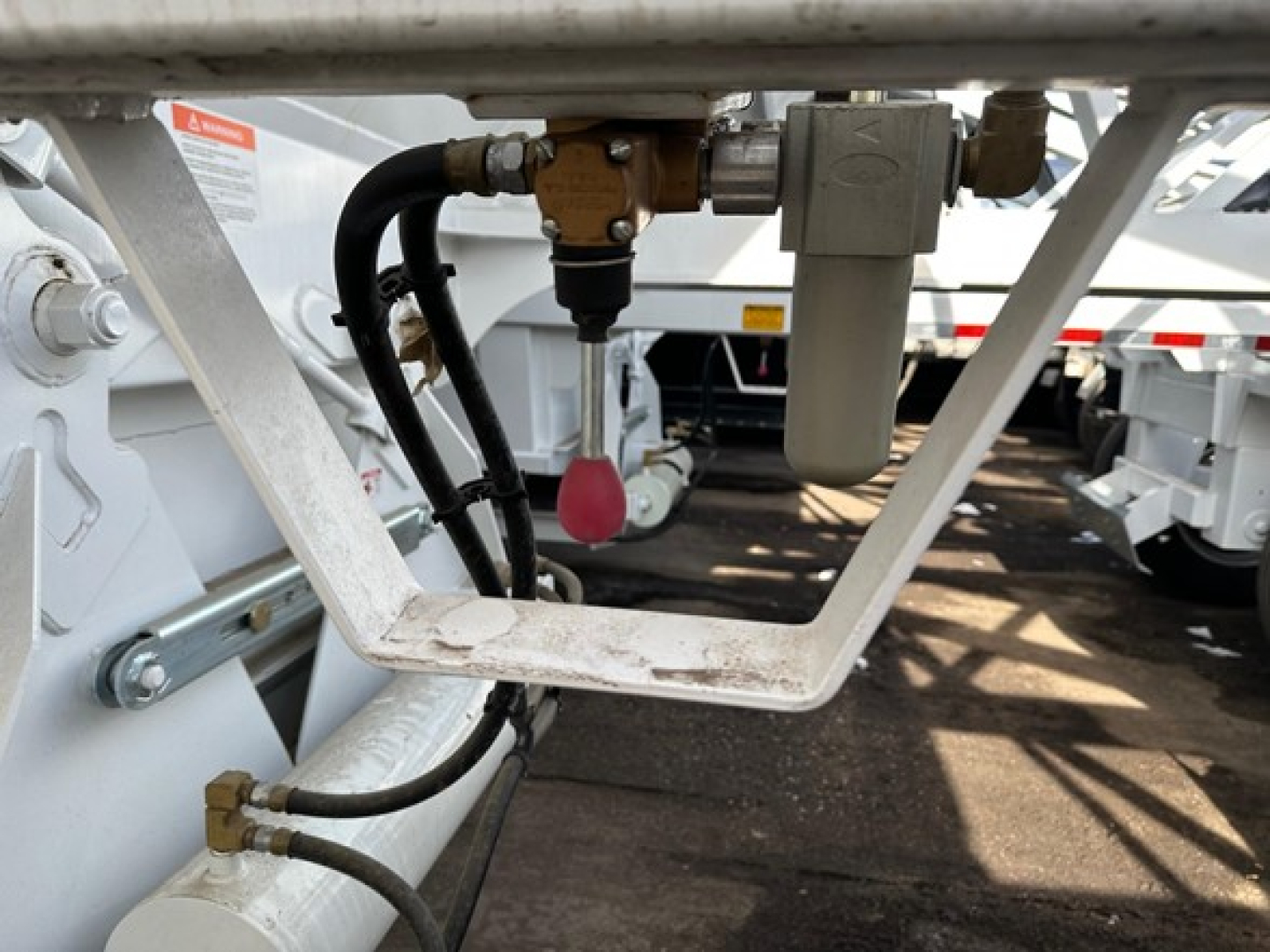 Bottom dump trailer undercarriage showing hydraulic lines, valve, and frame; close-up of control components and brackets.